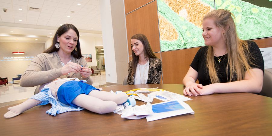 Image of two teens and older female at table with demonstration doll