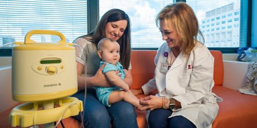 Photo of Ginger Carney in white coat talking to Melissa Groves, and 7-month-old St. Jude patient Nathan