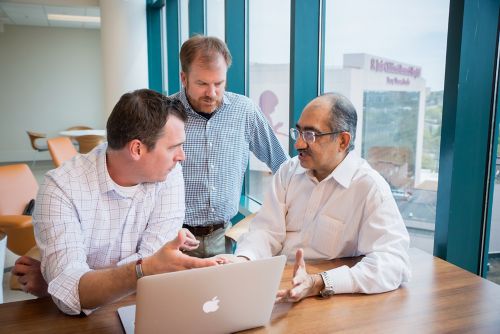 Three men talking in front of a computer