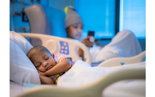 Little boy asleep in hospital bed with relative out of focus in background. 