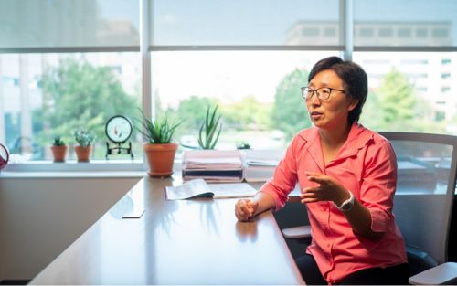 Image of Xinwei Cao, in orange shirt, sitting at table 