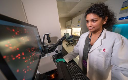 A female scientist stands in front of a computer monitor observing a microscopy image.