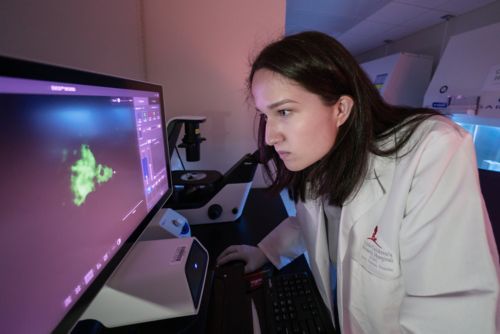 A female scientist looks at a computer screen to analyze a microscopy image.