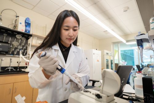 A female scientist stands at the bench in the lab and pipettes a liquid into a laboratory instrument.