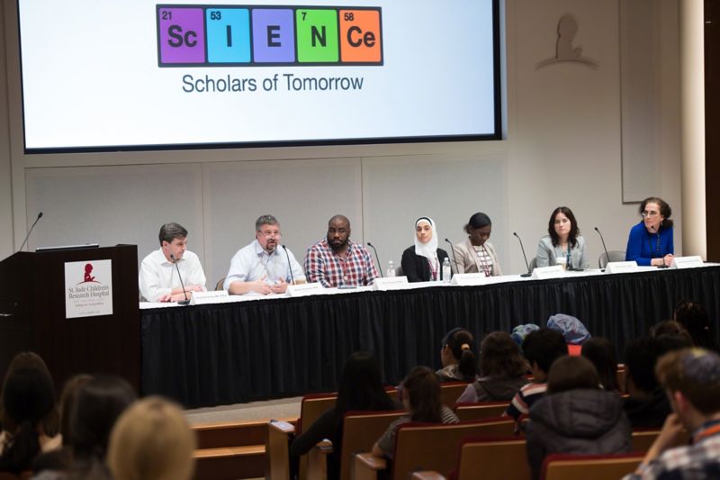 Photo of group of people sitting at table on a stage