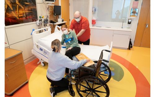 Caretaker using a sliding board to help female child in wheelchair