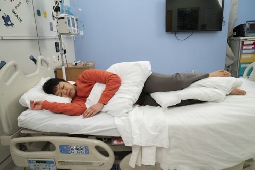Woman lying on side in hospital bed with pillow between legs.