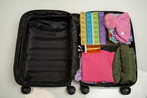 Suitcase packed for hospital with clothing, pill organizer, and prescription medication