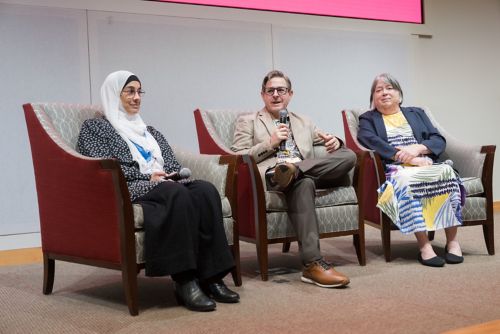 three people sitting in chairs on a stage.