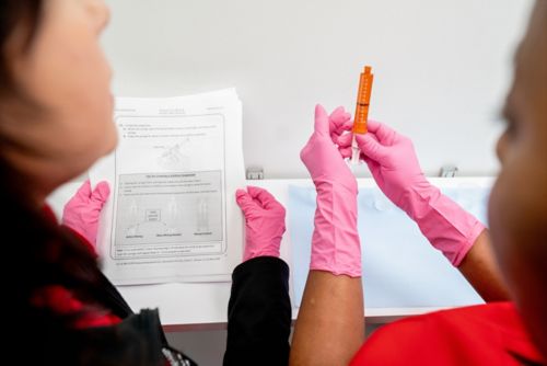 Two people with gloved hands examining a syringe and paperwork.
