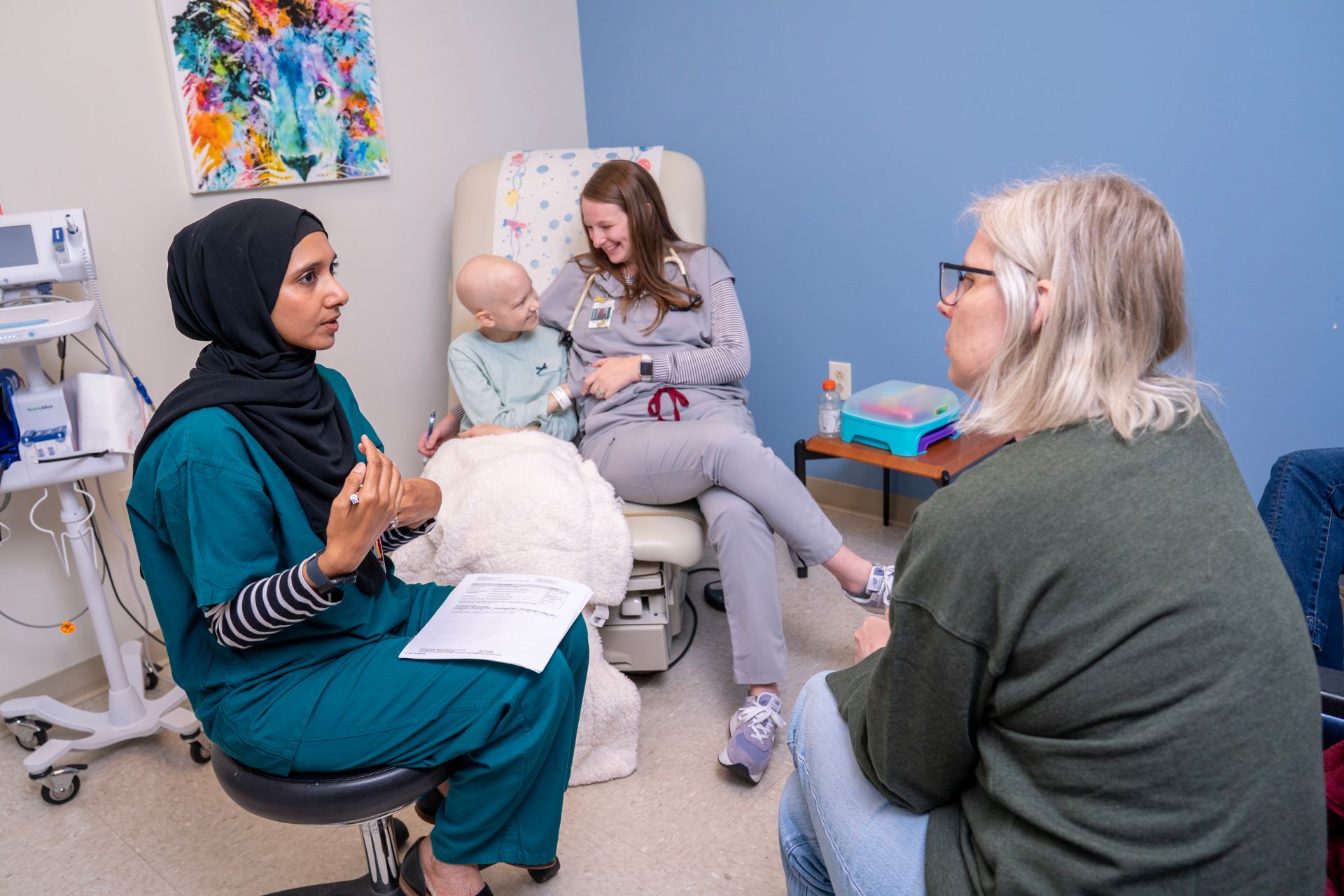 A doctor speaking with patient's mother, with patient and nurse in background
