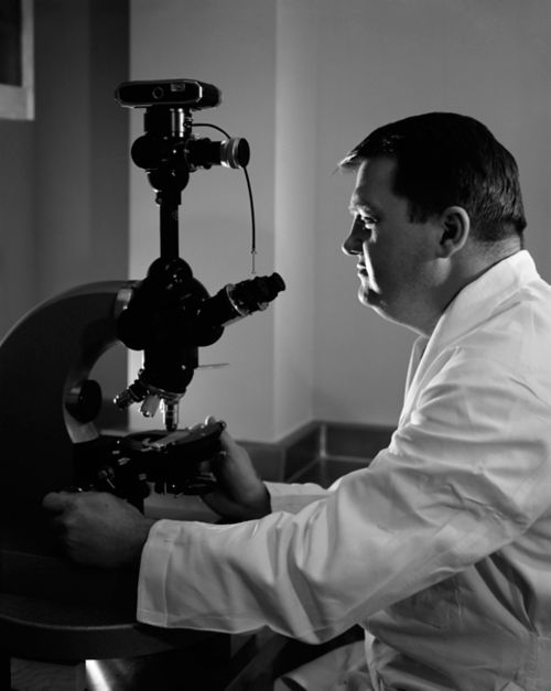 image of man in white coat working at microscope