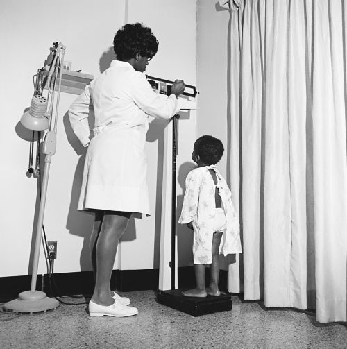 black and white photo of nurse weighing young child