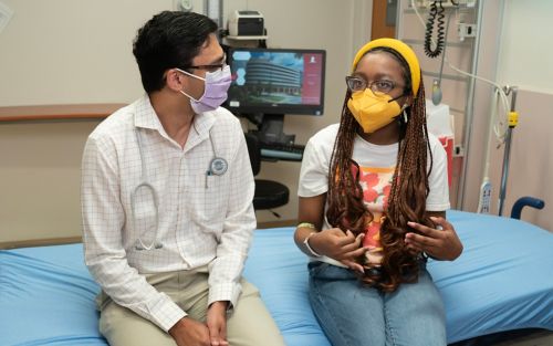 Female patient talking with doctor while sitting in hospital room wearing masks