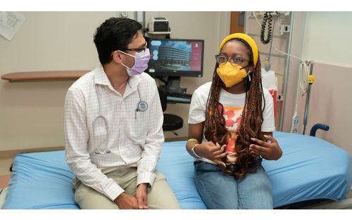 Female patient talking with doctor while sitting in hospital room wearing masks