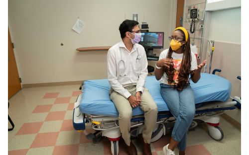 A man and a woman sitting on a hospital bed and talking to each other