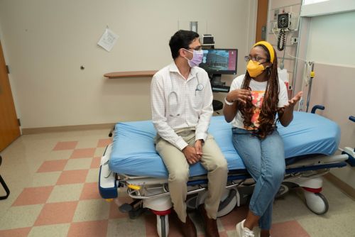 A man and a woman sitting on a hospital bed and talking to each other