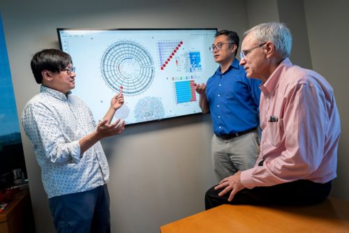 Three men talk in front of a screen displaying diagrams