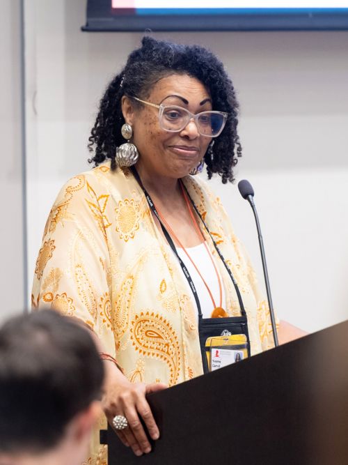 Yvonne Carroll, wearing yellow outfit, speaking at a podium