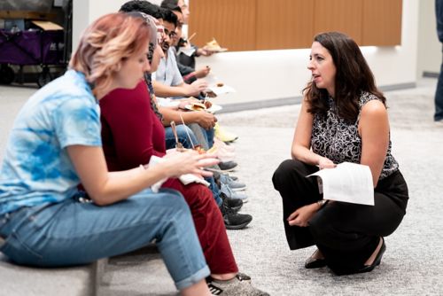Woman, kneeling, talks to group of seated students