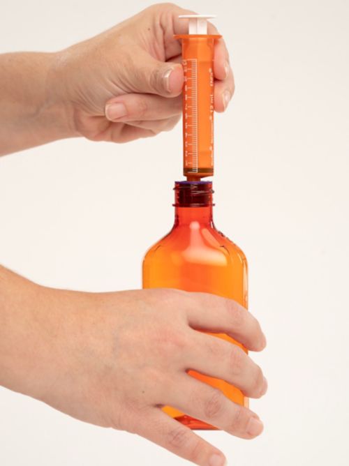 Person placing enfit syringe in fill cap of bottle