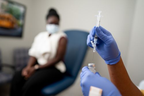 Women in exam room with hands in foreground with syringe and vial