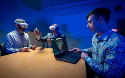 three men at a table, two using virtual reality headsets