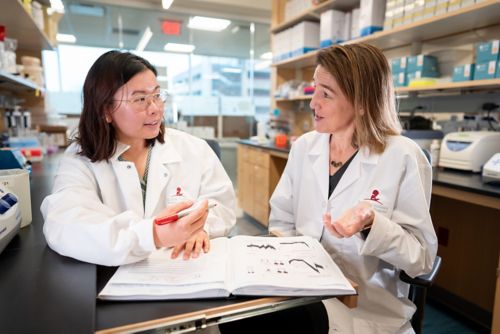 Two women in white coats talking in a lab