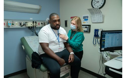 Image of man in examining room with nurse listening to his chest.