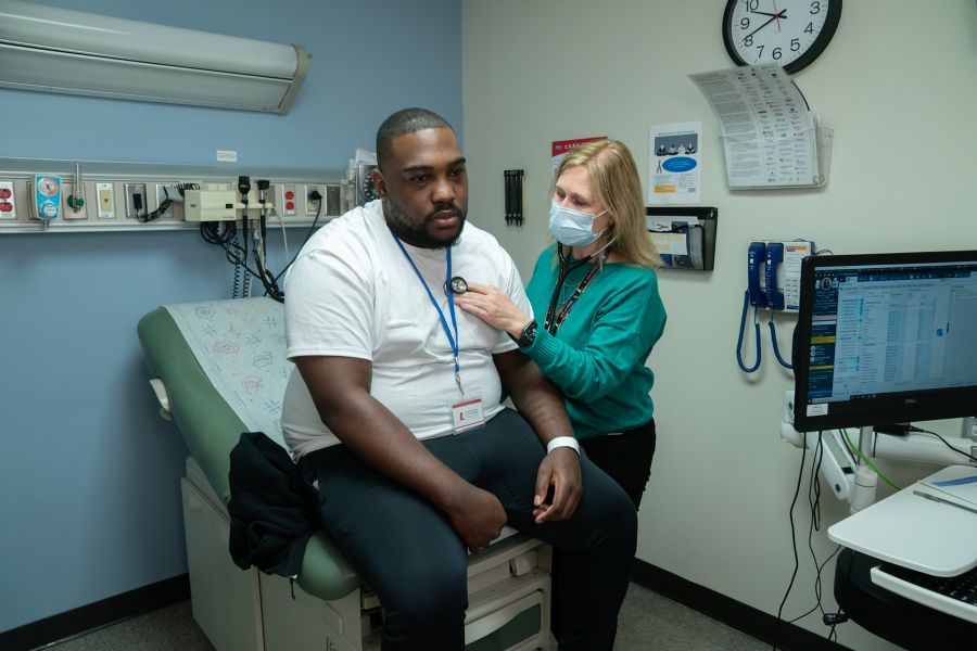 Female doctor listens to man's heart with stethoscope