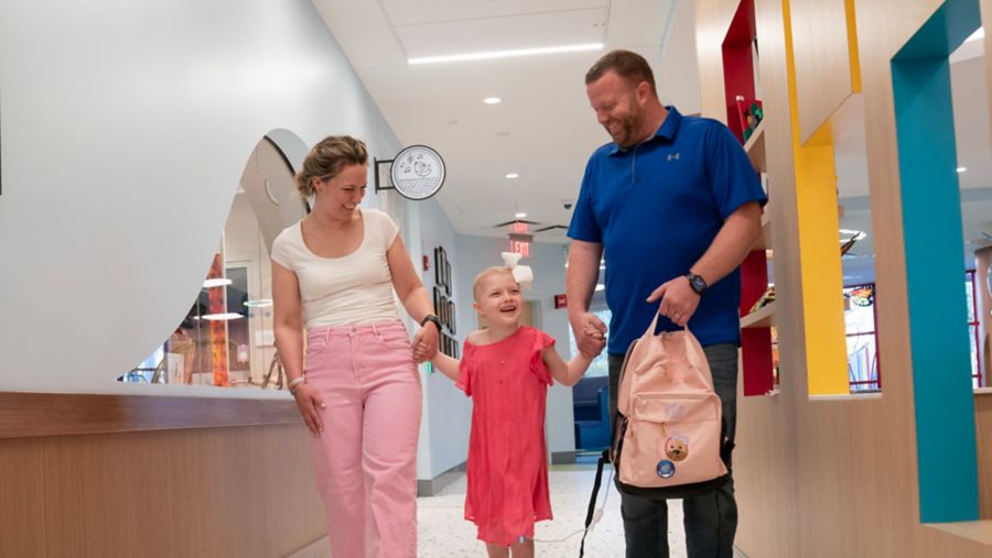 Parents walk with small female child in hallway at Family Commons