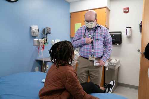 Man wearing mask talks to child in exam room