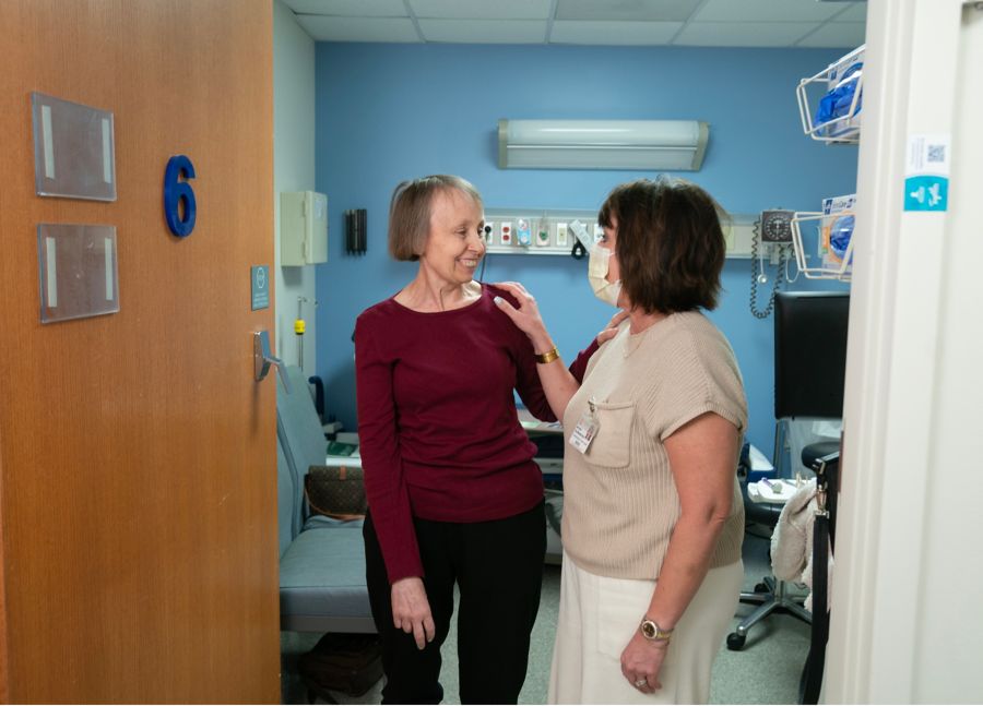 Two women conversing while standing in doorway of hospital room 