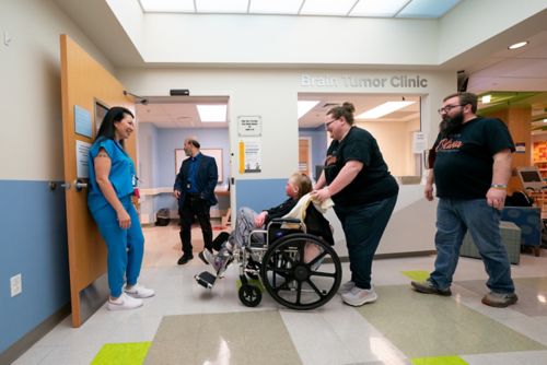 Girl in foreground being pushed in a wheelchair in a hospital hallway
