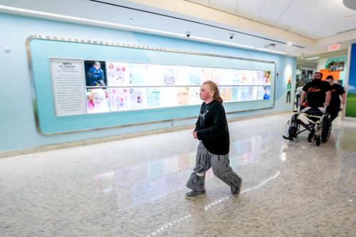 Girl in foreground walking through a hospital hallway