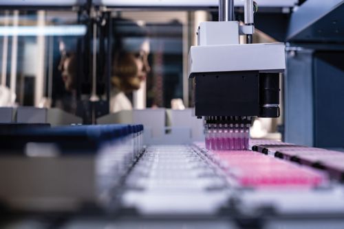 rows of laboratory vials with a woman in the background