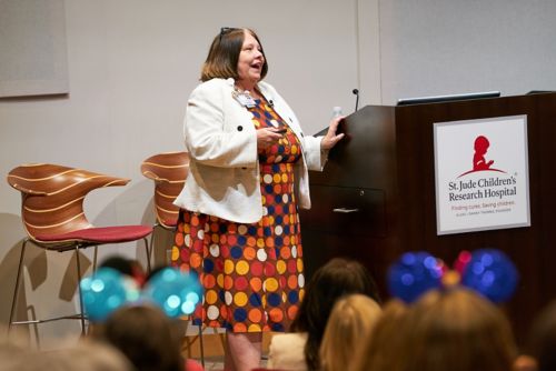 Woman wearing a polka dot dress speaks to crowd next to a podium
