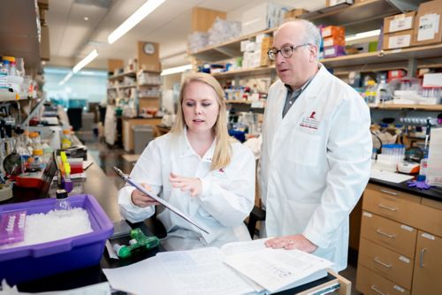 A man and woman in lab coats look at a piece of paper on a clipboard in a lab