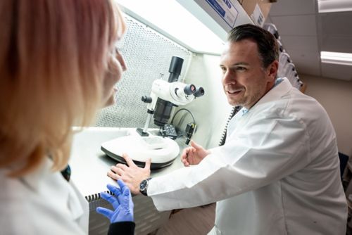 two men and a woman in lab coats talking in a lab