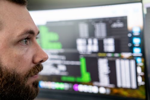 Side view of the face of a bearded man with computer screen in background