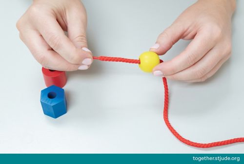 Person putting yellow bead on red shoe lace