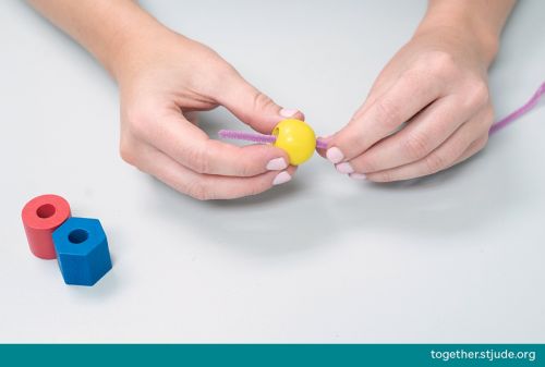 Person putting yellow bead on a pink pipe cleaner