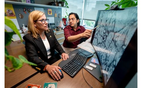 A woman and man looking at a computer screen that shows an image of cells