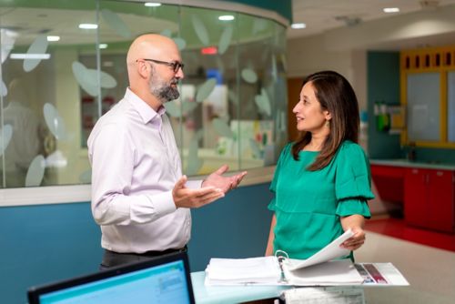 Man and woman standing next to table discussing the contents of a binder on the table