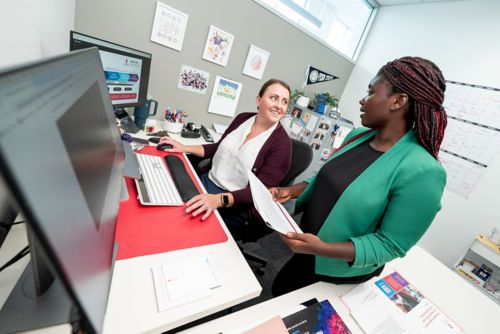 Two women talking in front of a computer monitor