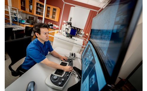 Man in blue shirt working at a computer with large screen monitor