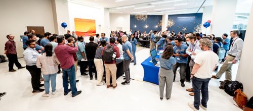 Large group of people standing around tables with computers in a lobby