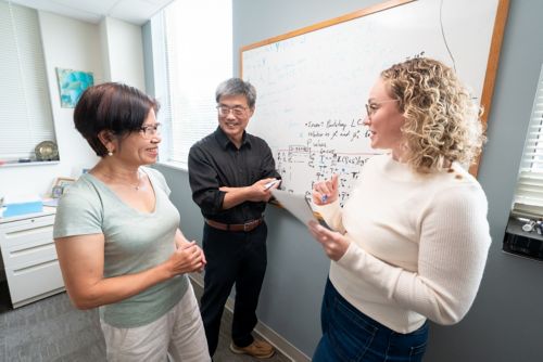 Two women and a man talking in front of a whiteboard.