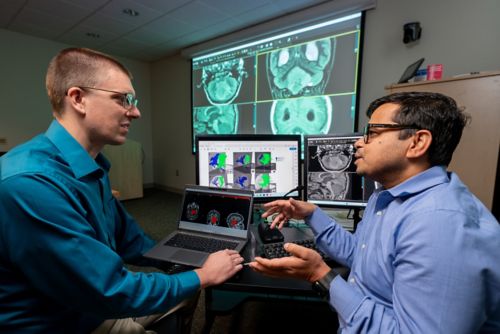 Asim Bag and member of his lab team talking in front of several computer screens showing various images of the brain