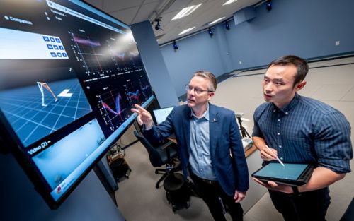 Two men looking at large, wall-mounted computer screen